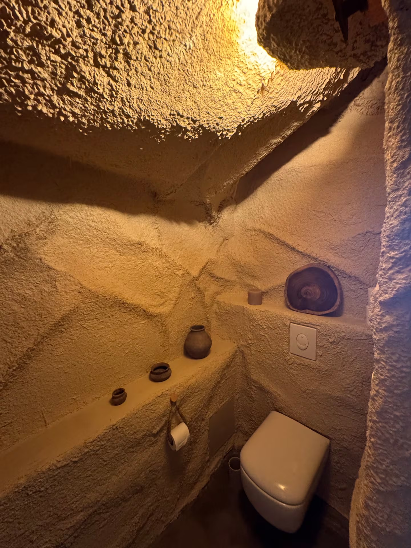 Toilettes troglodytes avec niches de pierre, poteries et bougie