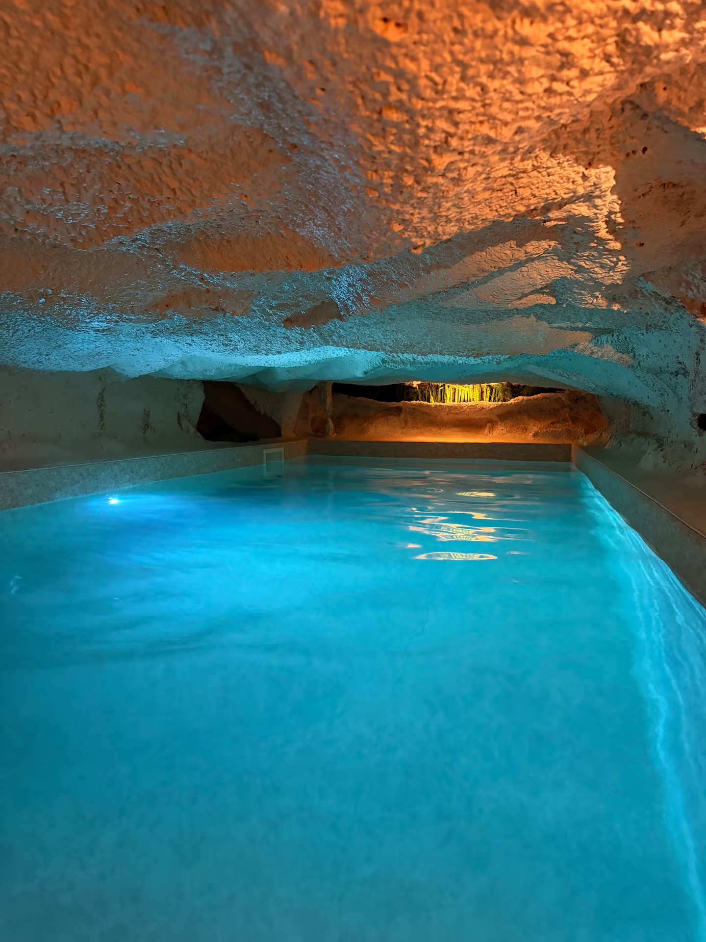 L'eau turquoise de la piscine s'enfonçant sous une voûte de calcaire éclairée d'ambre