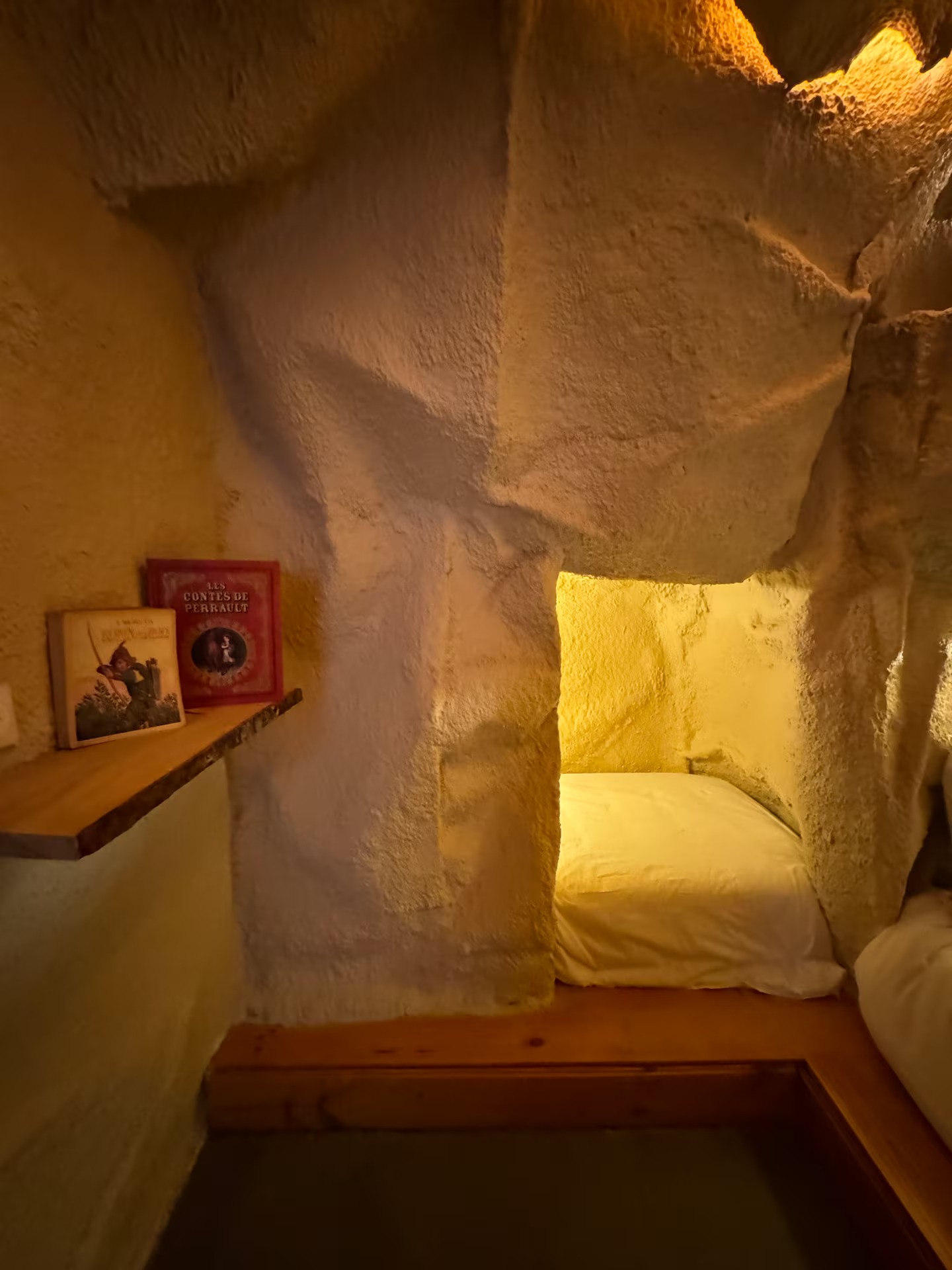 Alcôve-lit de la chambre 2, éclairée de doré, avec une étagère de livres de contes