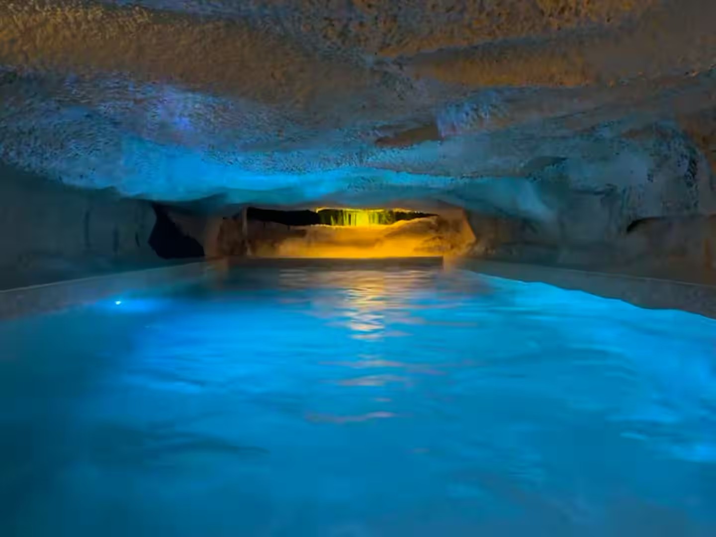 La piscine souterraine de La Grotte, éclairée de bleu et d'or sous la voûte de roche