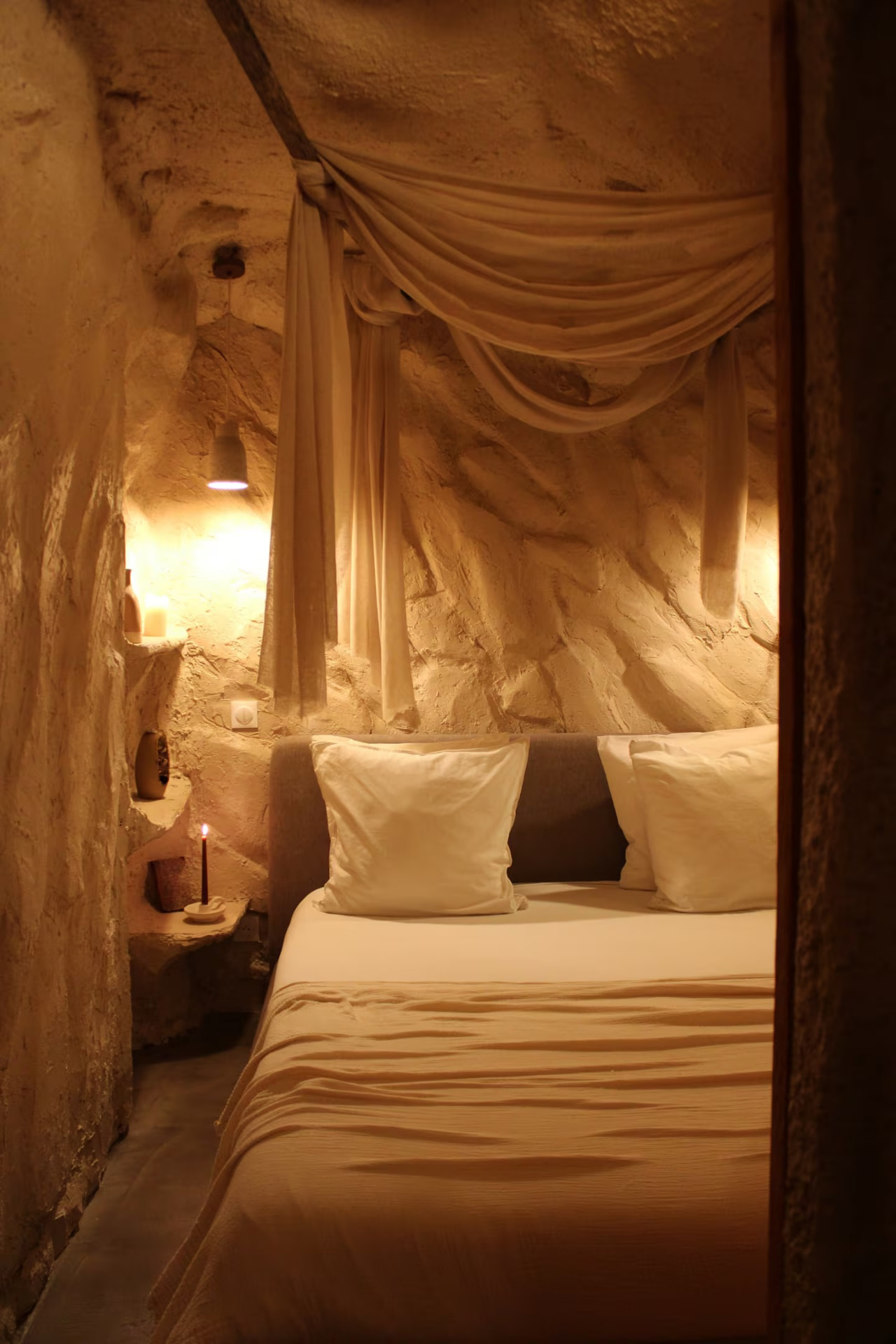 Chambre 1 : lit double sous un voilage, bougie allumée dans une niche de pierre